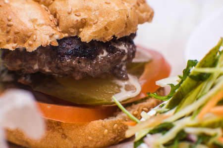 Classic american fast food background. Burger whole grain bun with grilled on barbecue meat and onions on wooden cutting board. Hamburger with fresh vegetables composition. closeupの写真素材