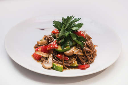 Buckwheat noodles with vegetables and mushrooms in round plate isolated on white background closeの写真素材