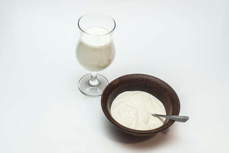 Glass goblet with milk and a bowl of sour cream on white backgroundの写真素材