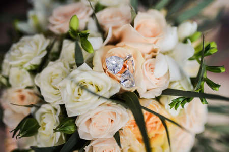 Silver earrings with diamonds bride lying on the bridal bouquet with white roses. Wedding accessories bride and groom before the ceremony photographedの写真素材