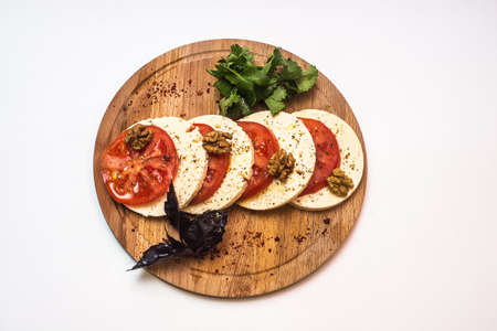 Pieces of round cheese and tomatoes with spices on a wooden board on a white backgroundの写真素材