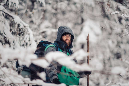 Portrait of smiling bearded man hiker, who relaxing in the winter forest. Toned image. Man with a beard tourist in a winter forest. Walks through the forest. Looks at the cameraの写真素材