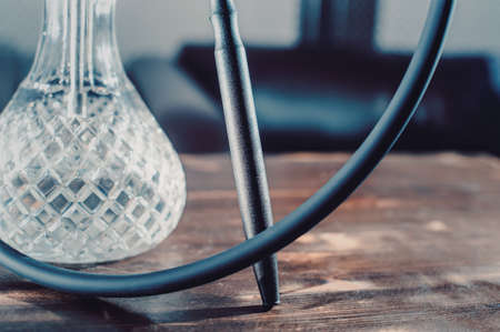 Crafted hand-made hookah stands on a wooden table in a hookah cafe on the background of the art wall. crystal type of shisha flask hookah closeupの写真素材