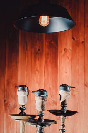 Crafted hand-made hookah stands on a wooden table in a hookah cafe on the background of the art wall. three old school hookahs bowls view closeの写真素材