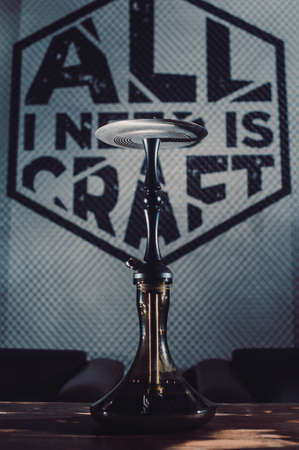 Crafted hand-made hookah stands on a wooden table in a hookah cafe on the background of the art wall. dark hookah with dark glass bulb on the table vertical viewの写真素材