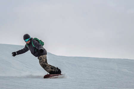 snowboarder in a black helmet riding on a snowy track. Snowboarder rides over fresh snow on the slope in winter, extreme sport. copy empty space. from afar view. closeの写真素材