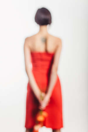 Brunette in a red dress with poppy flowers on a white background in the studio. stands on her feet back out of focus viewの写真素材