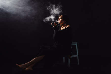 The brunette in a black sweatshirt is smoking a pipe in a cloud of smoke horizontalの写真素材