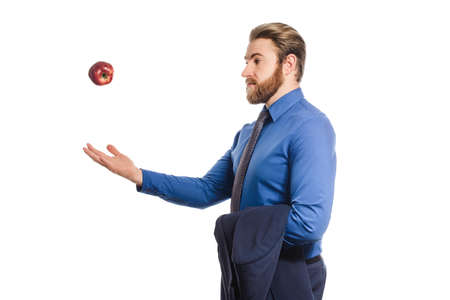 Handsome businessman in a blue business suit standing isolated against white background offers an apple. throws the fruit into the airの写真素材