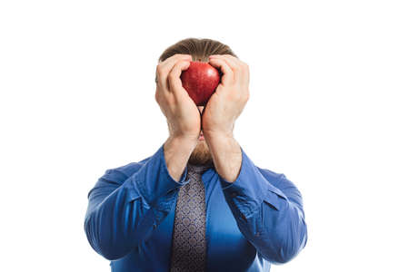 Handsome businessman in a blue business suit standing isolated against white background offers an apple. holds a fruit in two hands near the headの写真素材