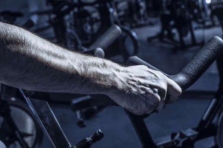 A bicycle simulator in the gym. Toned image. The  is exercising on a stationary bike. hands view from the sideの写真素材