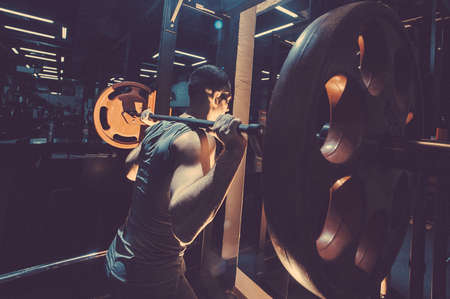 Cross training. Part of young man in sportswear lifting barbell at gym. Toned image. Young man crouches with a barbell. With a barbell on the shoulders back different viewの写真素材