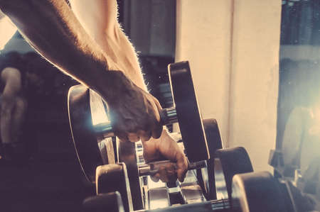 Athlete in the gym training with dumbbells. Toned image. Man is engaged with dumbbells on the bench. Hands with dumbbells. another view closeの写真素材
