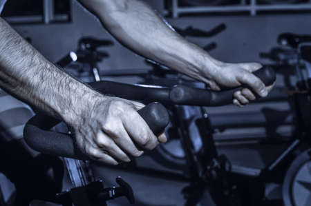 The guy is engaged in a bicycle simulator in the gym. Toned image. The guy is exercising on a...