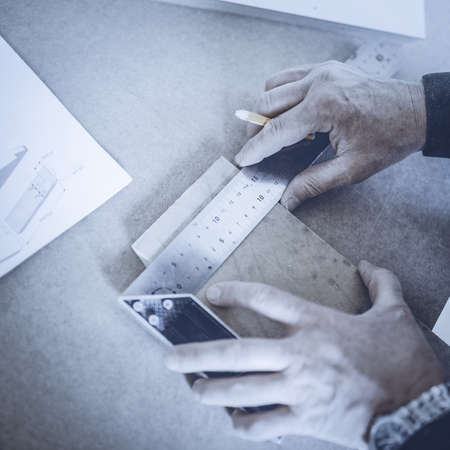 A carpenter uses a framing square for marking a hole in a furniture part. Toned image. puts the...