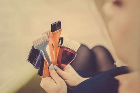 Professional hairdresser tools in the hands of the stylist. Toned image. Many brushes for dyeing hair in handsの写真素材