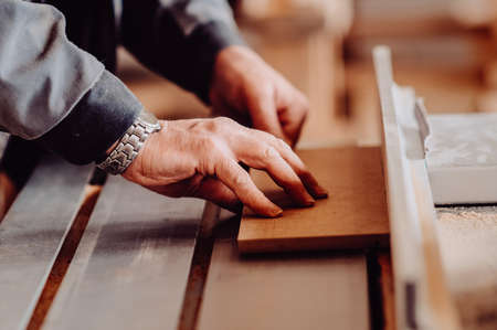 Carpenter working on woodworking machines in carpentry shop. Toned image. Man collects furniture boxes. Saws furniture details with a circular saw. close up viewの写真素材