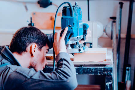 Worker uses a manual grinder. Toned image. Process of processing the edges of a furniture productの写真素材