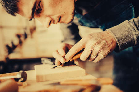 The carpenter uses a chisel for carving. Carving view. Toned image. from the front view with the faceの写真素材