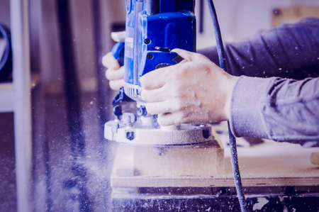 Worker uses a manual grinder. Toned image. Process of processing the edges of a furniture product. in side view horizontalの写真素材