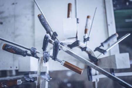 Gluing furniture parts with clamps and press. Toned image. Carpenter screw clamp tools pressing wood slats ang white glueの写真素材