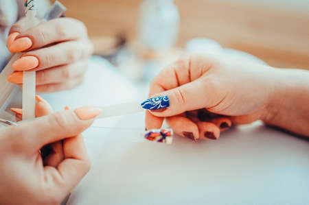 Female client during Gel Manicure with Manicurist Displaying Samples of Patterns on nails. Toned image. Selection of false nails in the beauty salonの写真素材