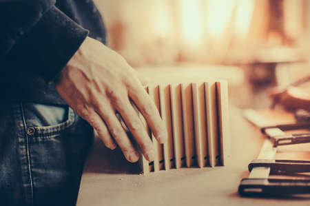 A carpenter works on woodworking the machine tool. Carpenter working on woodworking machines in carpentry shop. Toned image. Man collects furniture boxes. from the side viewの写真素材