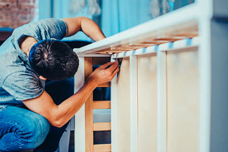 Joiner collects a new baby cot with a hand tool. carpenter collects a cot. Toned image. collects the walls of the crib using a hand hexagon. fixes the bottom of the crib to its walls. from afarの写真素材