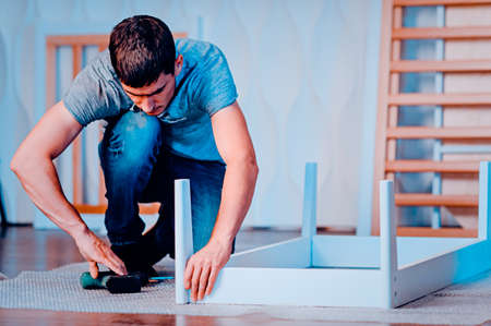 Joiner collects a new baby cot with a hand tool. carpenter collects a cot. Toned image. collects the...