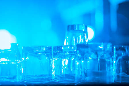 Party concept. Many clean washed glasses for strong drinks on the bar in the blue light. blurred image. Toned image. ready for a partyの写真素材