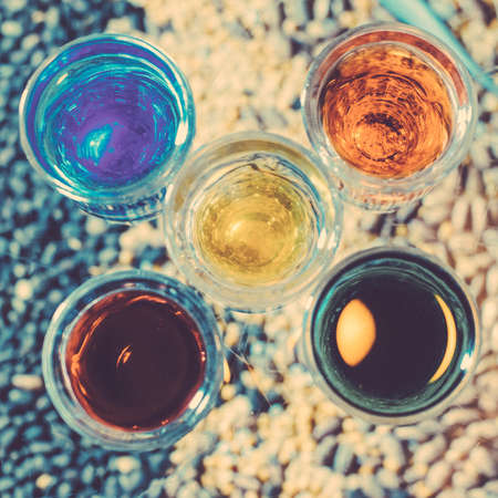 Party and holiday celebration concept. Toned image. Image of multicolored liqueurs in glasses on a wooden stand behind the bar with blurred background. from the top square cropping.の写真素材