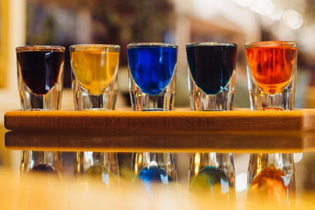 Party and holiday celebration concept. Image of multicolored liqueurs in shots on a wooden stand behind the bar. close upの写真素材