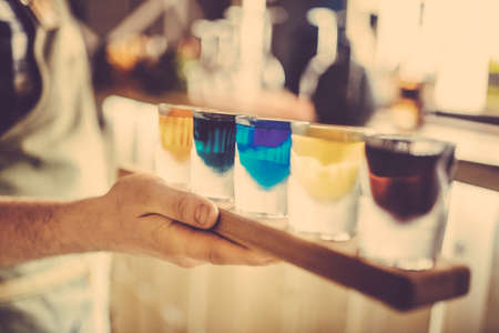 Party and holiday celebration concept. Toned image. Image of multicolored liqueurs in frozen glasses on a wooden stand behind the bar with blurred background. from the sideの写真素材