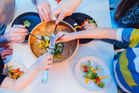 healthy food, family, children, hapiness and people concept - happy family with two kids making and eating fresh salad at home. bowl with salad and many hands from the top close viewの写真素材