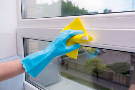 a gloved hand holds a yellow sponge, cleaning, washing windowsの写真素材