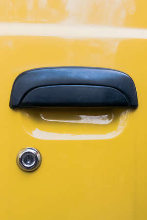 Black doorknob and silver lock of a yellow car. Vertical orientation.