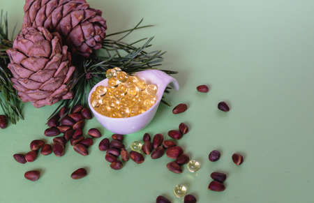 Cones and cedar seeds and oil in capsules lies in a white ceramic spoon on a greenの写真素材