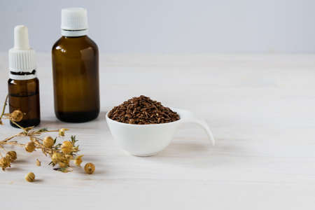 Dark bottles with flax oil, seeds in a spoon and a dry stalk of flax on a light wooden table.