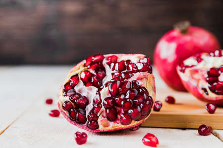 Whole fruit and halves of ripe pomegranate lie on a table on a wooden background. Juicy fresh...