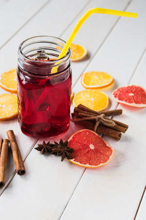Glass cup with a red drink on a light background, next to pieces of dried orange, lemon, grapefruit, cinnamon and anise. A warming winter drink. Vertical orientationの写真素材