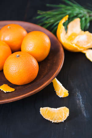 Fresh whole and peeled tangerines lie on an old clay plate on a dark backgroundの写真素材