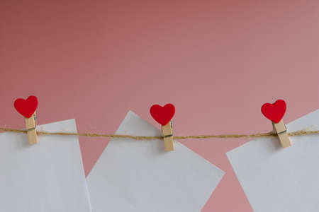 Blank message card attached with a wooden clothespin with a red heart on a rope on a pink backgroundの写真素材