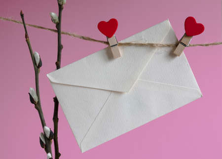 An empty cardboard envelope is hung with wooden clothespins with a red heart and a willow branch on...