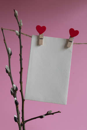 An empty cardboard envelope is hung with wooden clothespins with a red heart and a willow branch on a pink background. Easter holiday conceptの写真素材