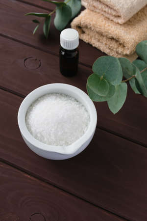 A branch of eucalyptus and essential oil in a bottle, sea salt and beige towels on a wooden background.の写真素材
