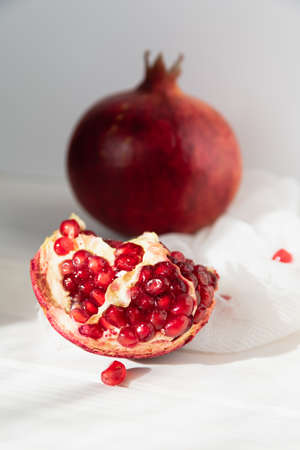 Whole fruit and halves of ripe pomegranate lie on a table on a wooden background. Organic Bio fruits. Minimalistic still life in bright colorsの写真素材