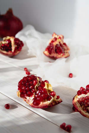 Pieces of ripe pomegranate fruit lie on a table on a white wooden background. Juicy fresh pomegranates. Organic Bio Fruits. Vertical orientation.の写真素材