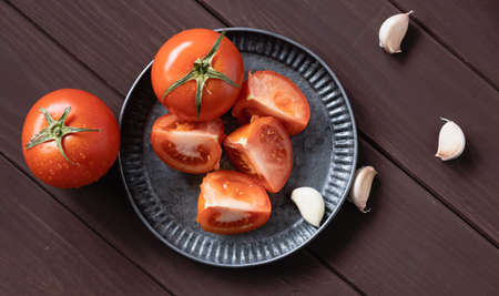 Slices of garlic and slices of tomato and whole fruits lie on a plate and are scattered on a wooden table top view. Background of the kitchen table.の写真素材