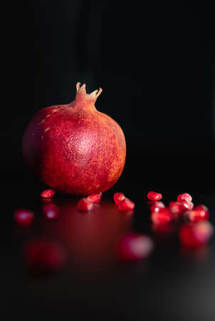 Ripe pomegranate fruit on a black background and pomegranate seeds are scattered on a dark background. Postcard, still life, background, texture. Bright fruit.の写真素材