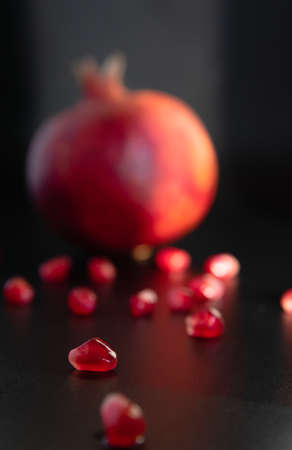Closeup pomegranate seeds and pomegranate fruit in the background on a dark. Selective focus Contrast. Red and black. Minimalistic still life.の写真素材